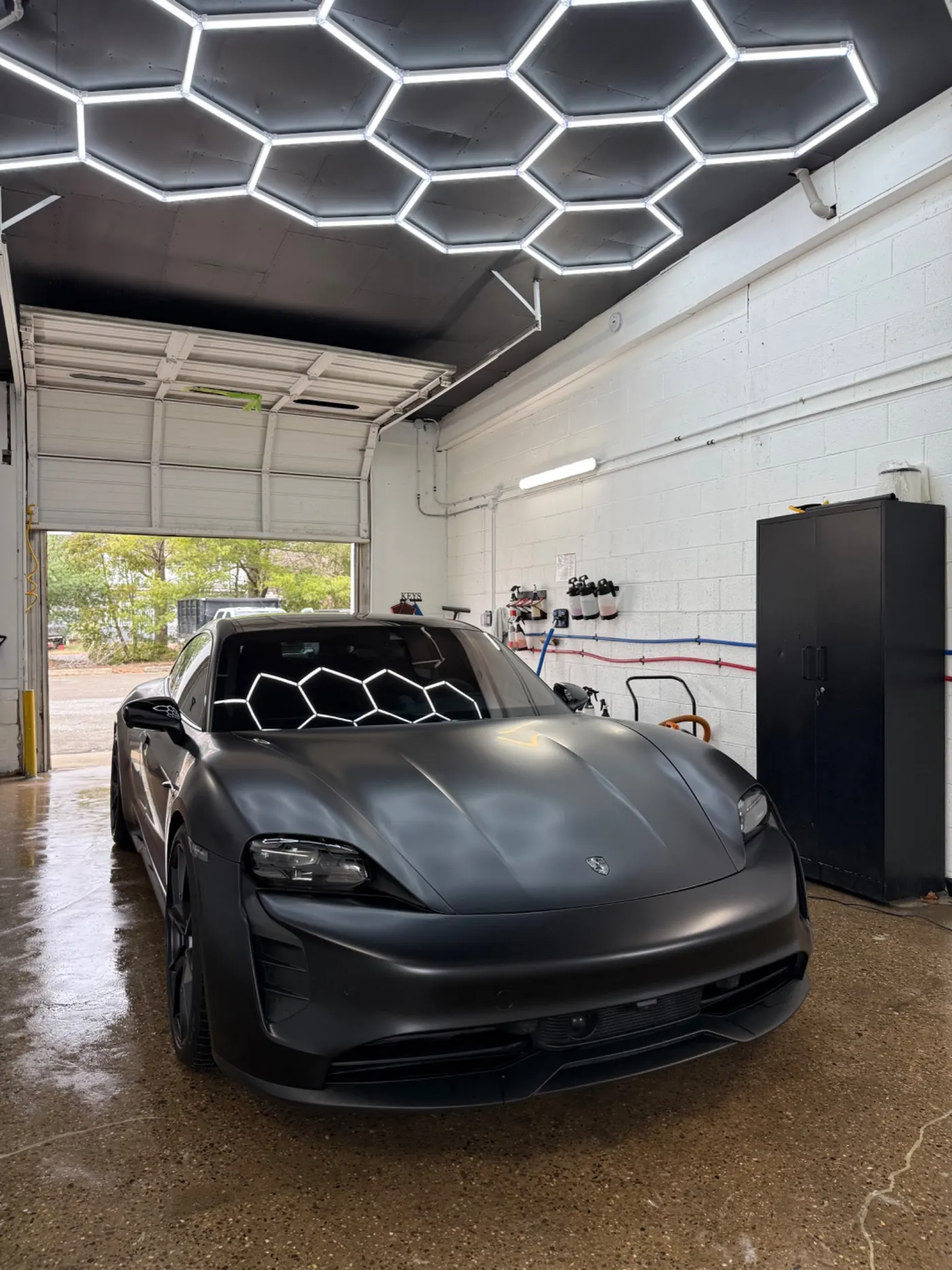 Matte gray Porsche in the Wash Haus bay beneath hexagonal lights